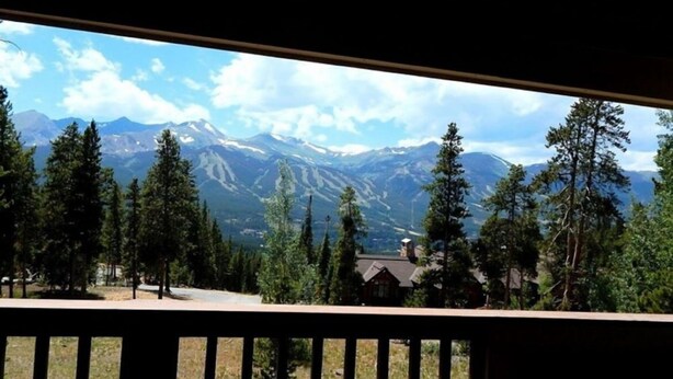 Une vue sur la montagne depuis un balcon doté d’une balustrade en bois, entouré d’arbres et d’un petit bâtiment.