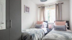 Ein Schlafzimmer mit zwei Betten, einem Kleiderschrank, einem Fenster mit Vorhängen und einem Nachttisch mit Lampe.