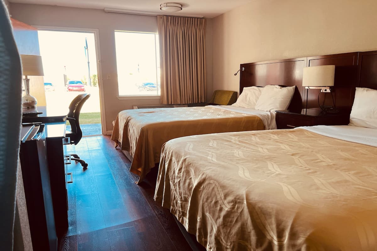 Une chambre d’hôtel avec deux lits, un bureau, une chaise, une lampe et une fenêtre avec des rideaux.