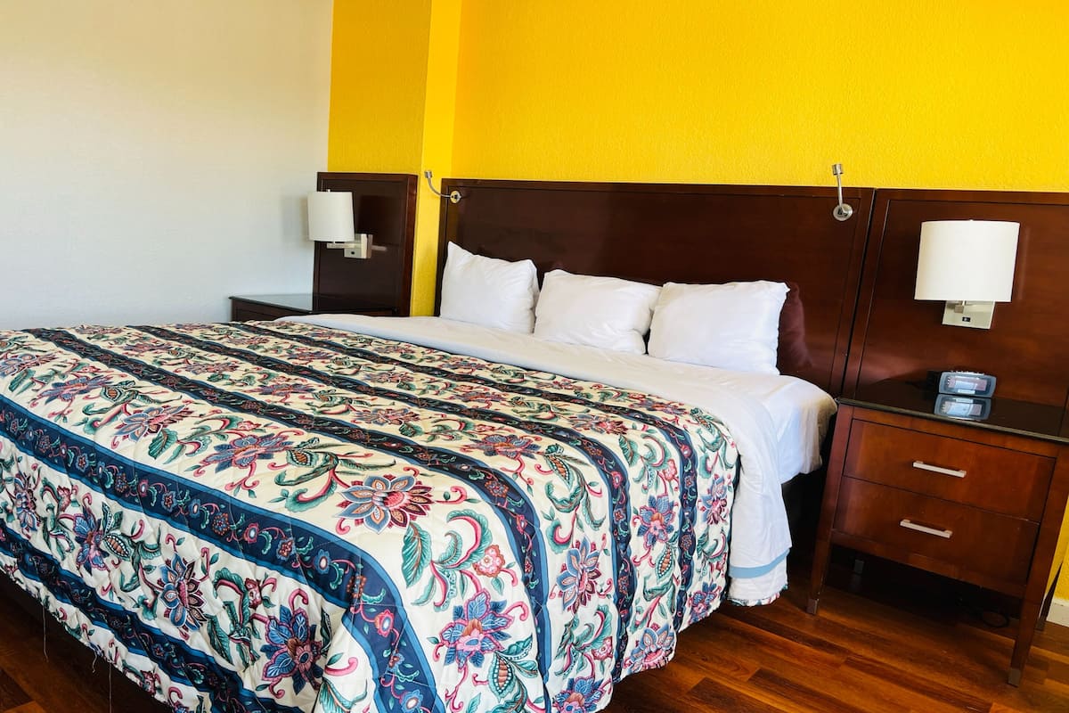 Une chambre d’hôtel avec un grand lit, une tête de lit en bois, deux tables de chevet avec des lampes et une petite table de nuit avec une lampe.