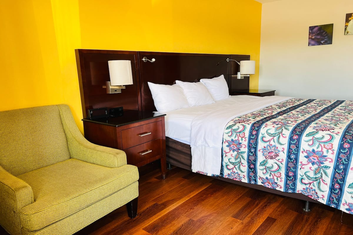 Une chambre d’hôtel avec un lit, une table de chevet, une lampe, une chaise et un plancher en bois.