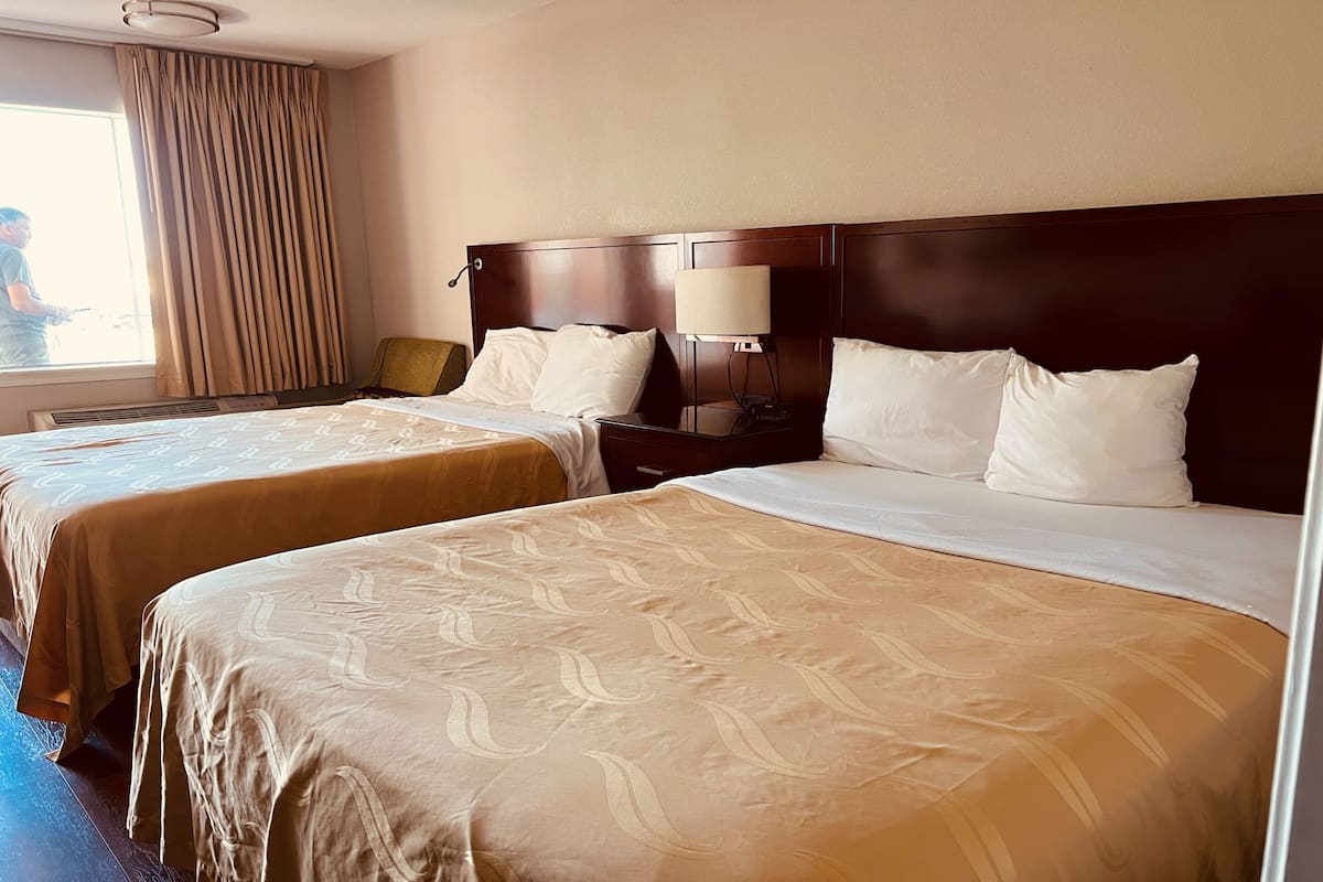 Une chambre d’hôtel avec deux lits, une table de chevet, une lampe et une fenêtre avec des rideaux.