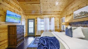 Ein Schlafzimmer einer Holzhütte mit einem Bett, einer Kommode, einer Bank, einem Fernseher und einem Gemälde an der Wand.