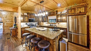 Eine holzgetäfelte Küchenzeile im Chalet-Stil mit einer Kochinsel, Barhocker, Edelstahlgeräten und einem großen Kühlschrank.
