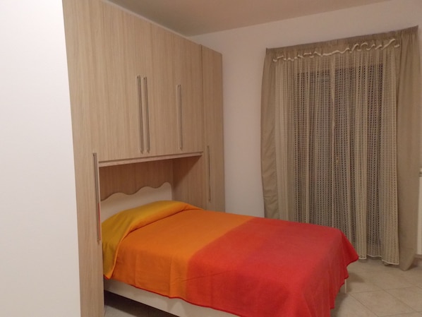 A bedroom with a bed, wooden wardrobe, and a window with patterned curtains.