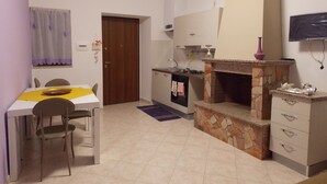A compact kitchen with a dining area, a stone fireplace, and a TV mounted on the wall. - Malu's House (Castelluccio Superiore)