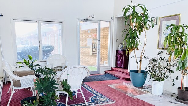 A spacious room with a large window, wicker chairs, a red patterned rug, and several potted plants. - Super9 inn (Albion)