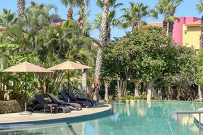 Ein Poolbereich mit Liegestühlen und Sonnenschirmen, umgeben von Palmen und viel Grün.