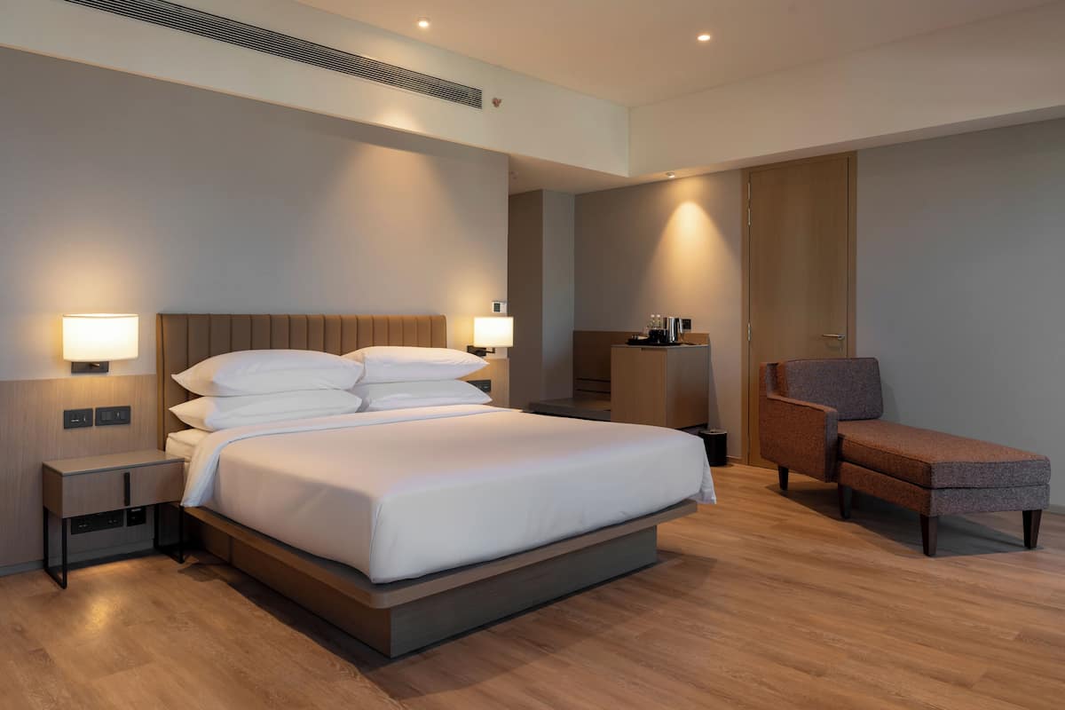 Une chambre d’hôtel moderne, dotée d’un grand lit, de lampes de chevet, d’une table de chevet, d’une chaise et d’un bureau avec une lampe.