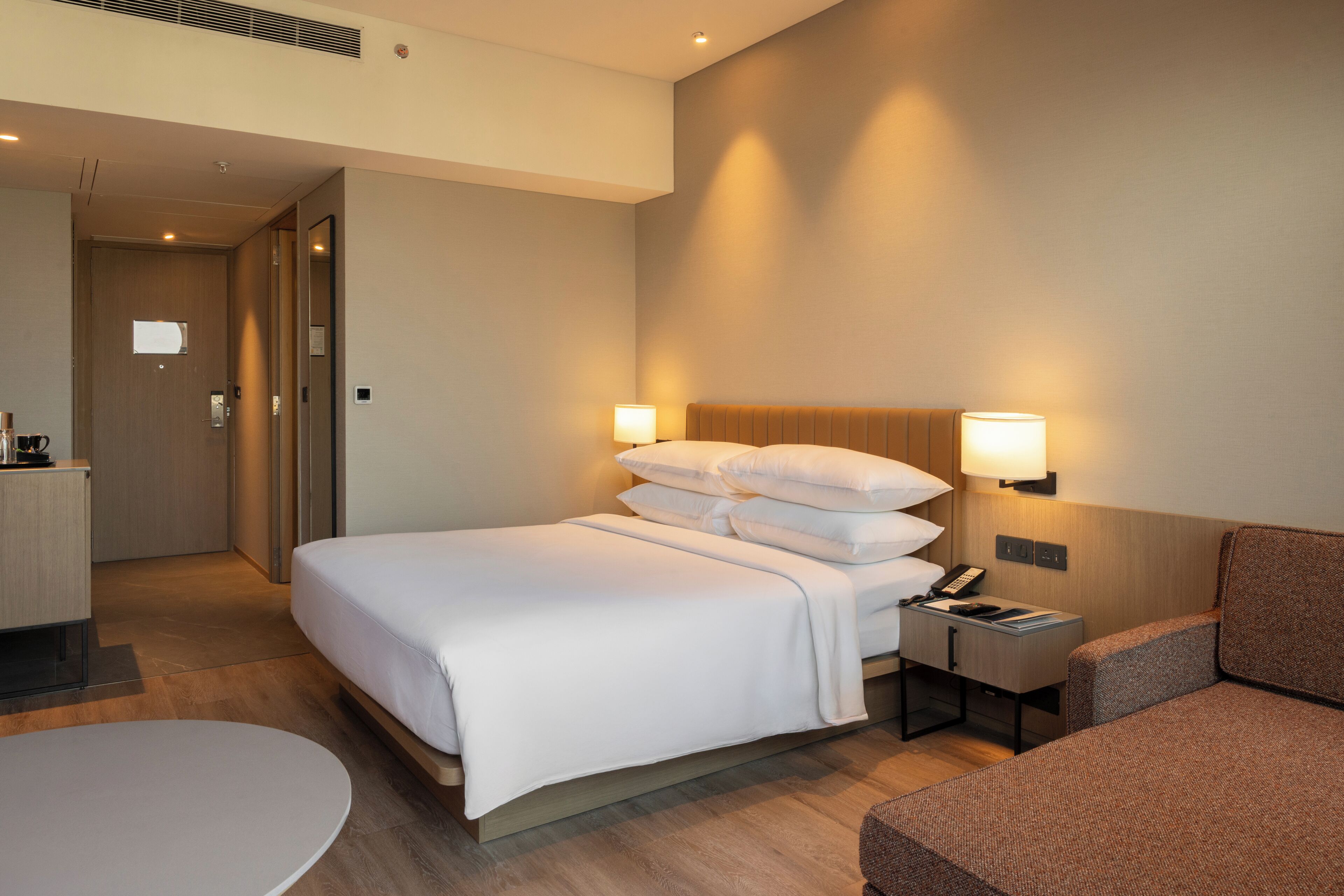 Een hotelkamer met een bed, nachtkastje, lamp en een zithoek.