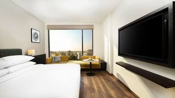A hotel room with a bed, a sofa, a TV, and a city view.