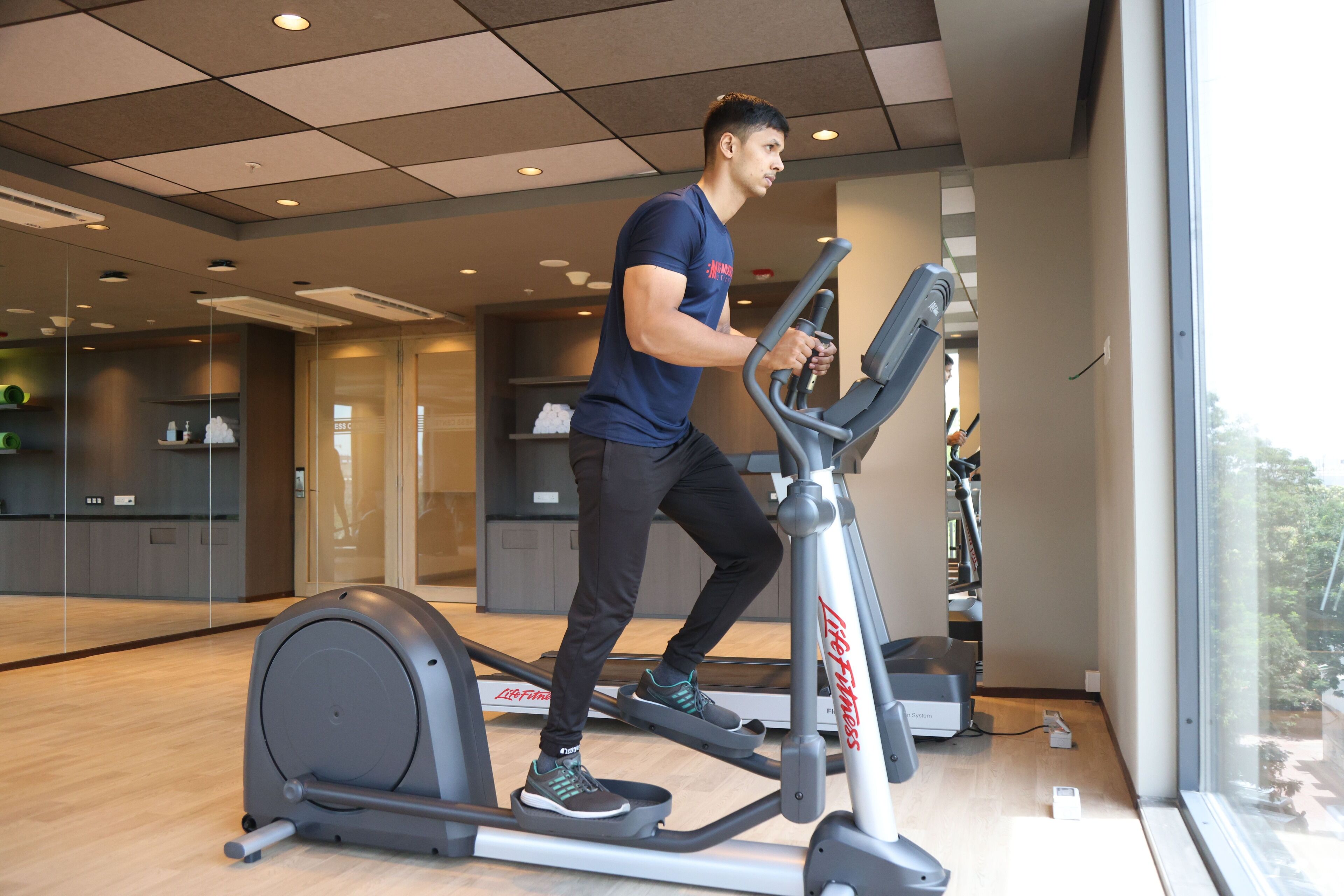 A man using an elliptical machine in a gym with a large window and a view of the outdoors.