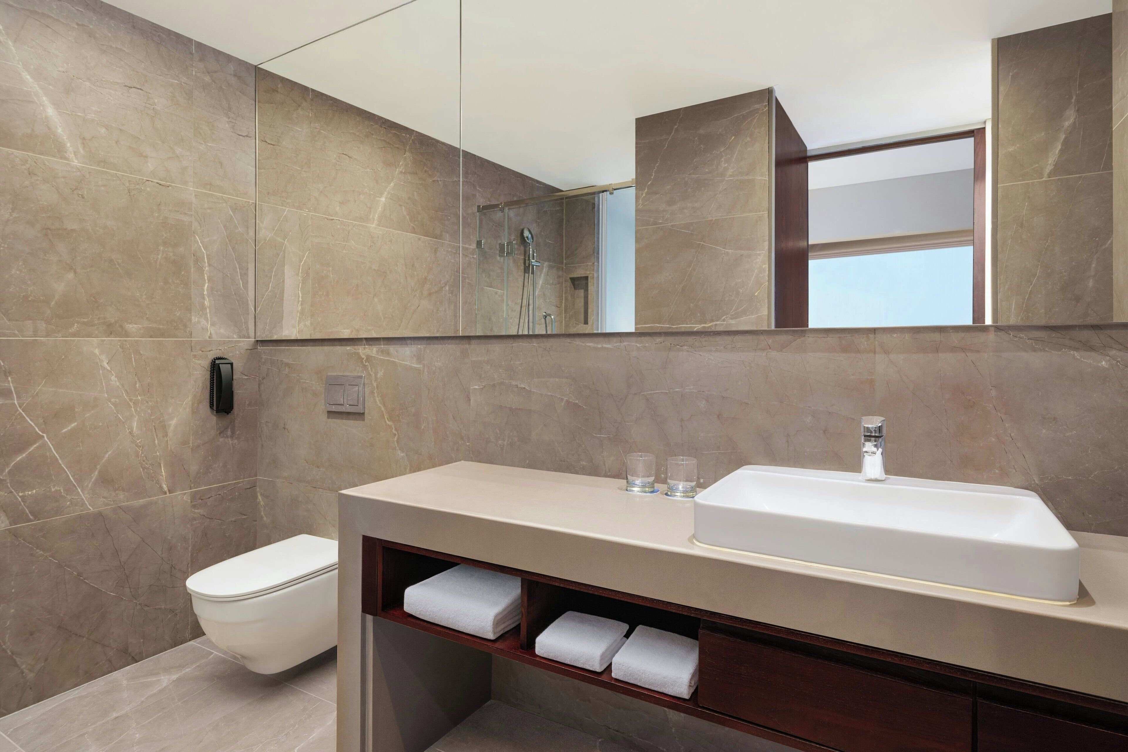 A modern bathroom with a marble wall, a white sink, a toilet, and a mirror.