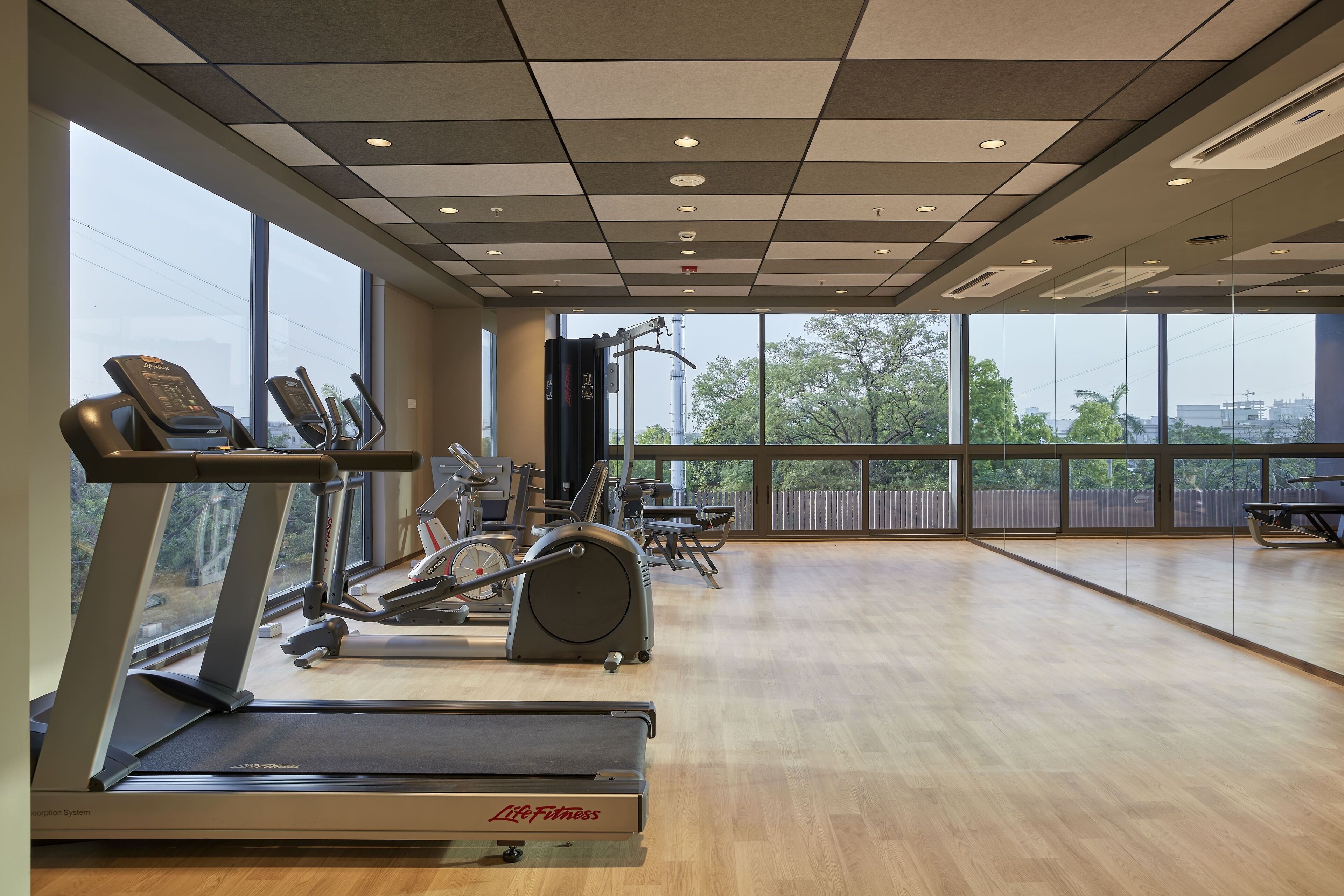 A gym with treadmills, elliptical machines, and a large window offering a city view.