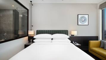 A hotel room with a large bed, a bedside table with a lamp, a small table with a phone, a sofa, and a window with a view.