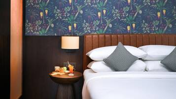 Habitación de hotel con cama, mesita de noche, lámpara y pared decorada con un estampado floral tropical.