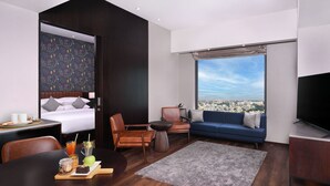 Una habitación de hotel moderna con cama, sofá, televisión y vista a la ciudad.