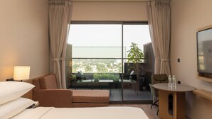 Habitación de hotel con cama, sofá, una mesita, televisor y balcón con vistas a la ciudad.