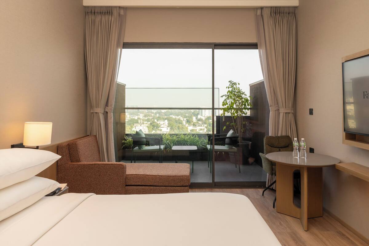 Une chambre d’hôtel comprenant un lit, un canapé, une petite table, une télévision et un balcon avec vue sur la ville.