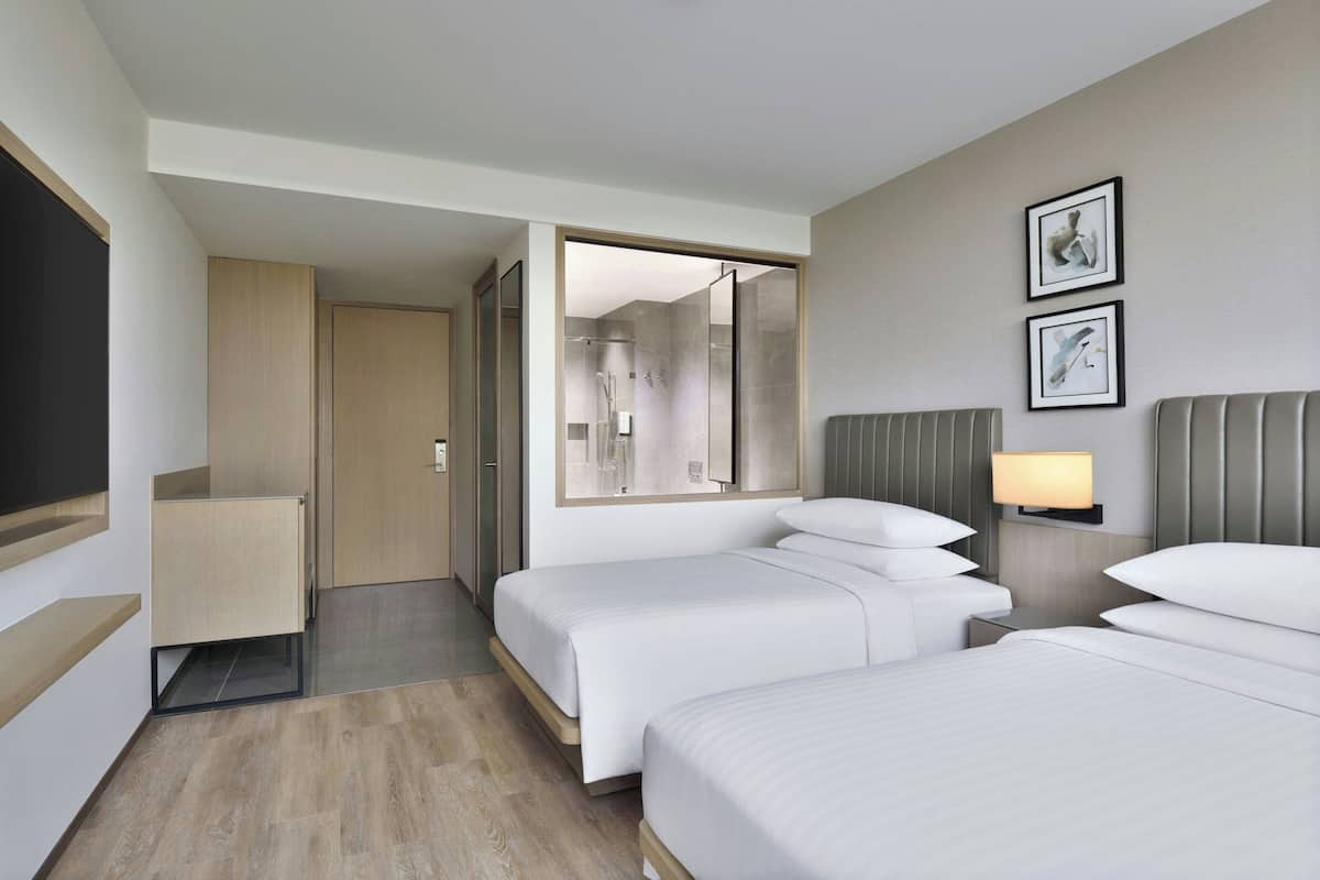 Une chambre d’hôtel avec deux lits, une table de chevet avec une lampe, un grand miroir et une armoire.