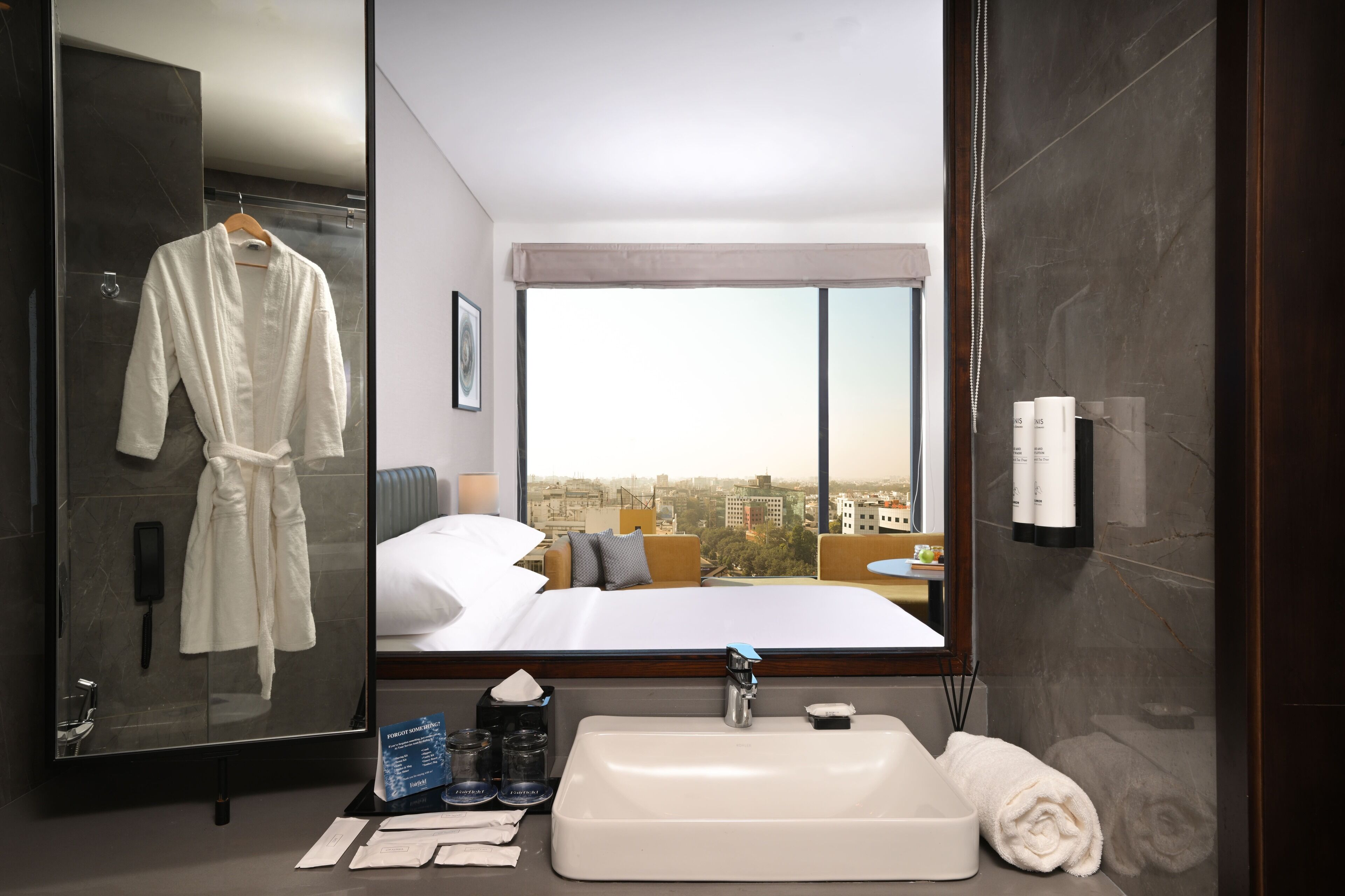Habitación de hotel con una cama grande, baño con lavabo y vistas de la ciudad a través de un ventanal.