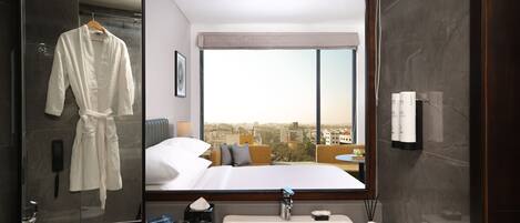 A hotel room with a large bed, a bathroom with a sink, and a view of the city through a large window.