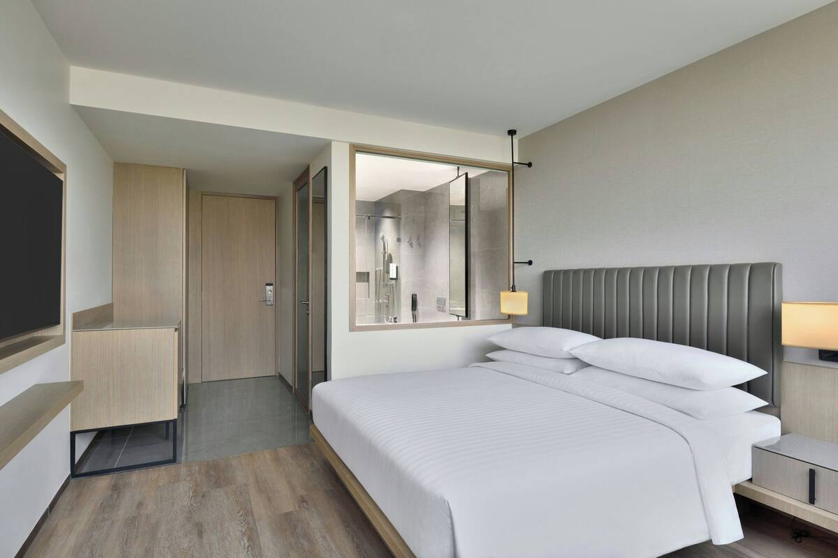 Une chambre d’hôtel moderne avec un grand lit, une table de chevet, un miroir et une armoire.