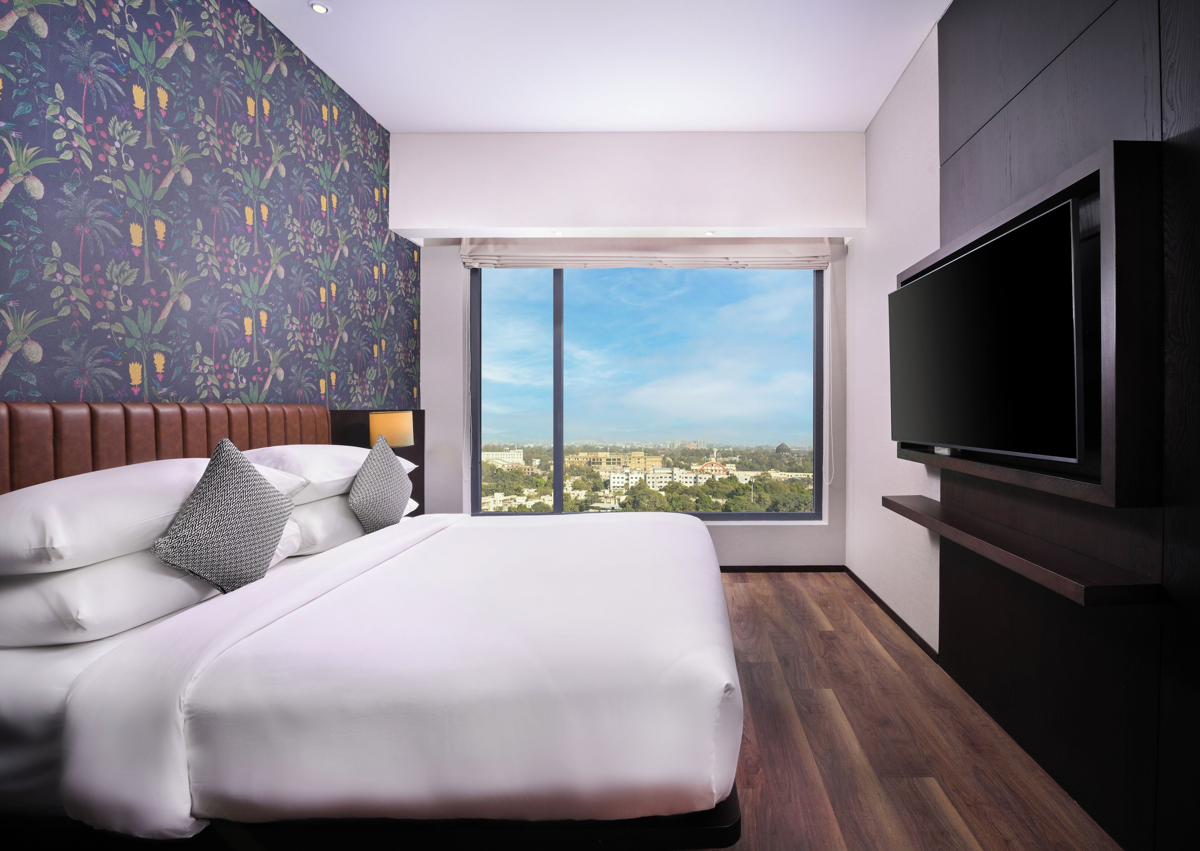 A modern hotel room with a large bed, a TV, and a city view.