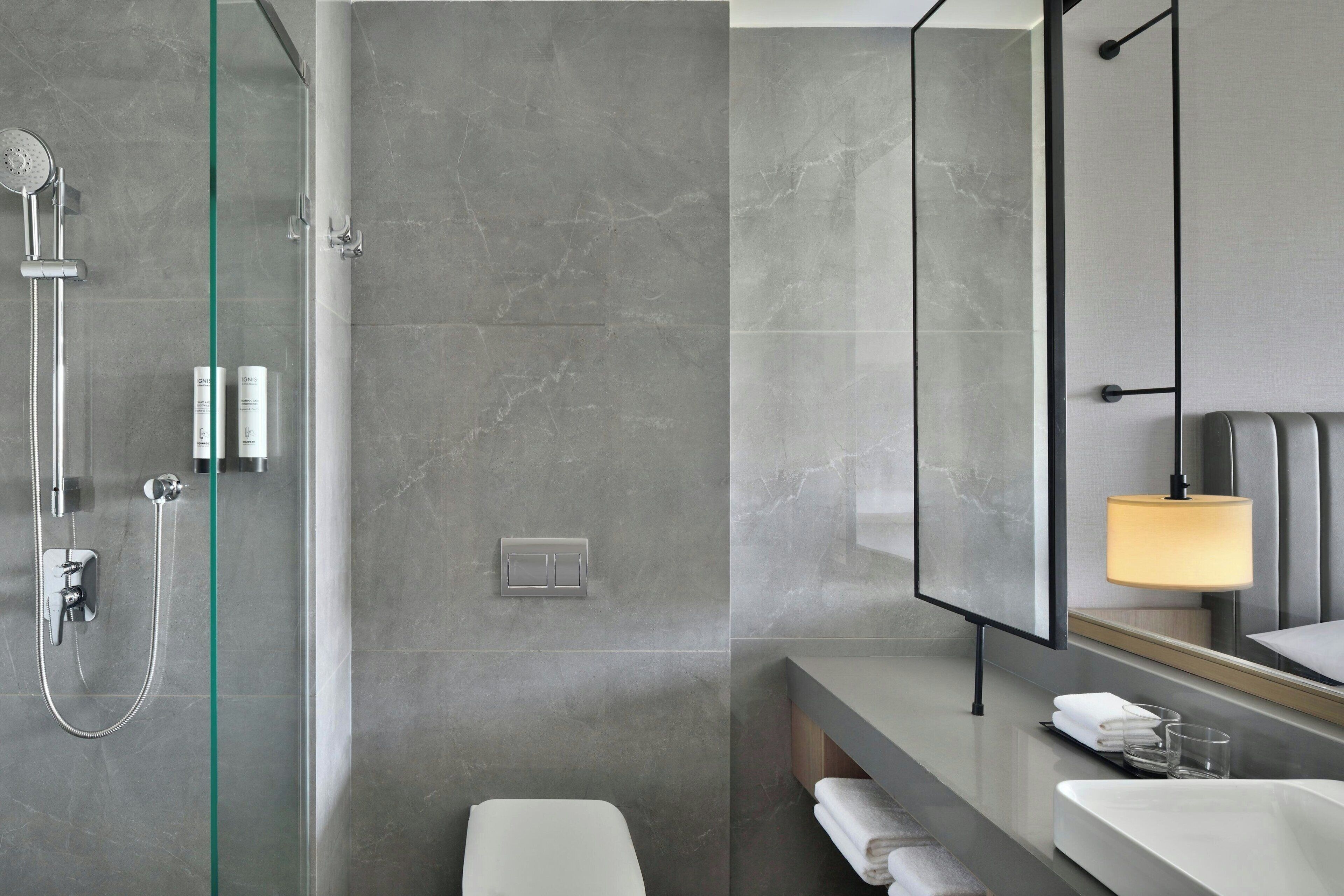 Un baño moderno con cabina de ducha de vidrio, un espejo grande y tocador con lavabo y toallero.