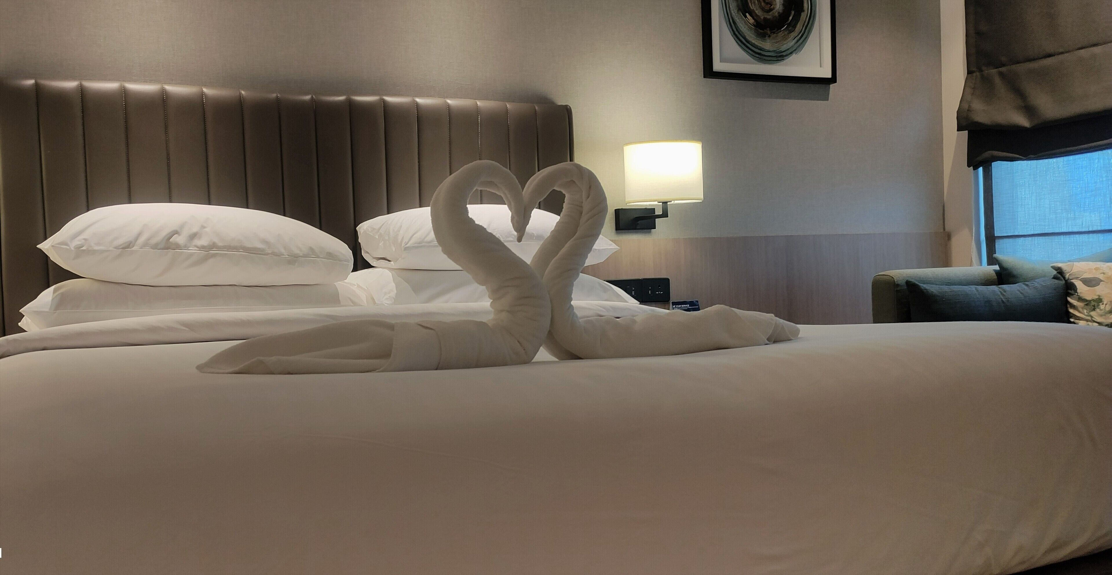 Una cama bien hecha con sábanas blancas y dos almohadas con forma de cisne.