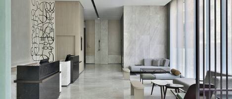 A modern hotel lobby with a reception desk, seating area, and large windows.
