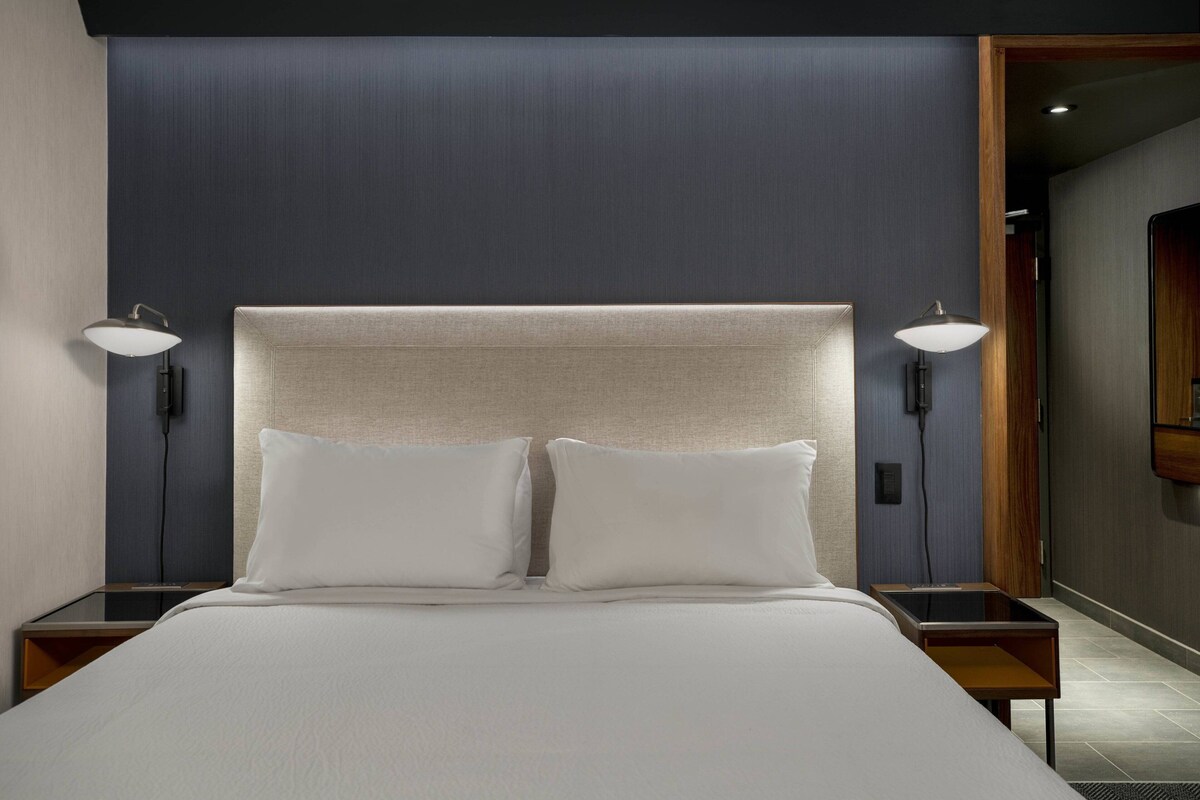 A hotel room with a large bed, two bedside tables, and two wall-mounted lamps.
