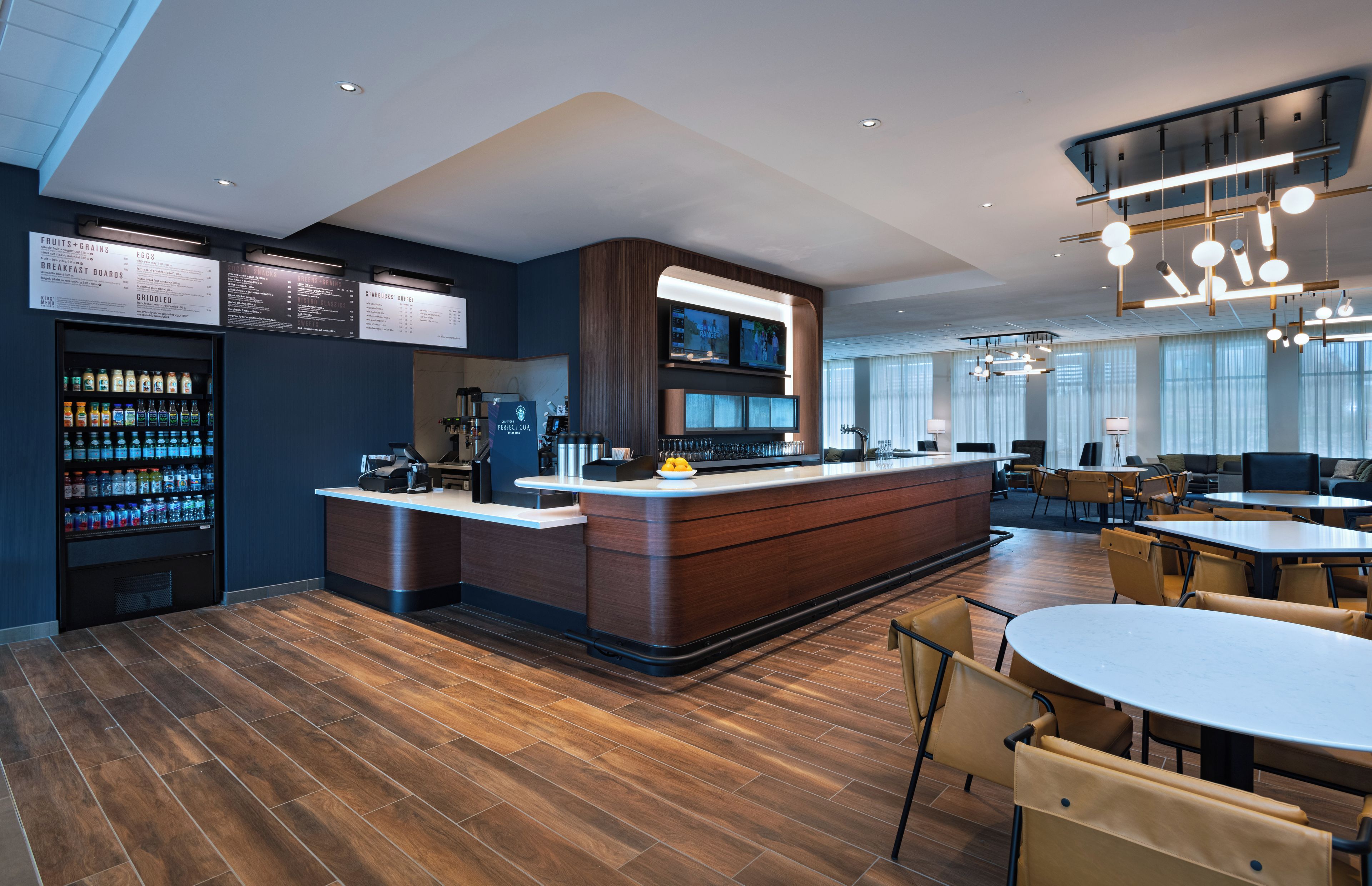 Un hall d’hôtel moderne avec un bar central, des espaces aménagés pour s’asseoir et un panneau affichant le menu.