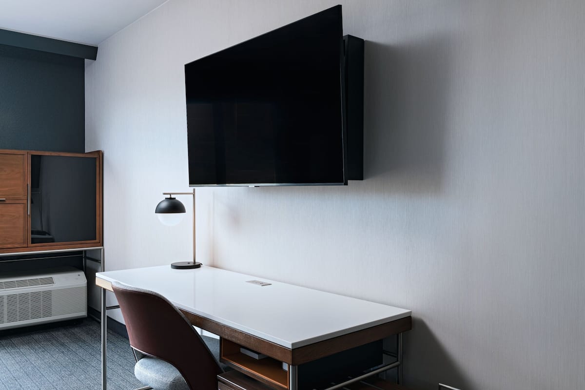 A modern room with a white desk, a brown chair, a mounted TV, and a wooden cabinet.
