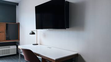 A modern room with a white desk, a brown chair, a mounted TV, and a wooden cabinet.