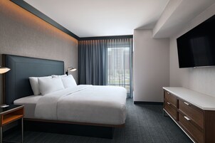 Una habitación de hotel moderna con una cama grande, un televisor de pantalla plana, un aparador de madera y vistas a la ciudad desde la ventana.