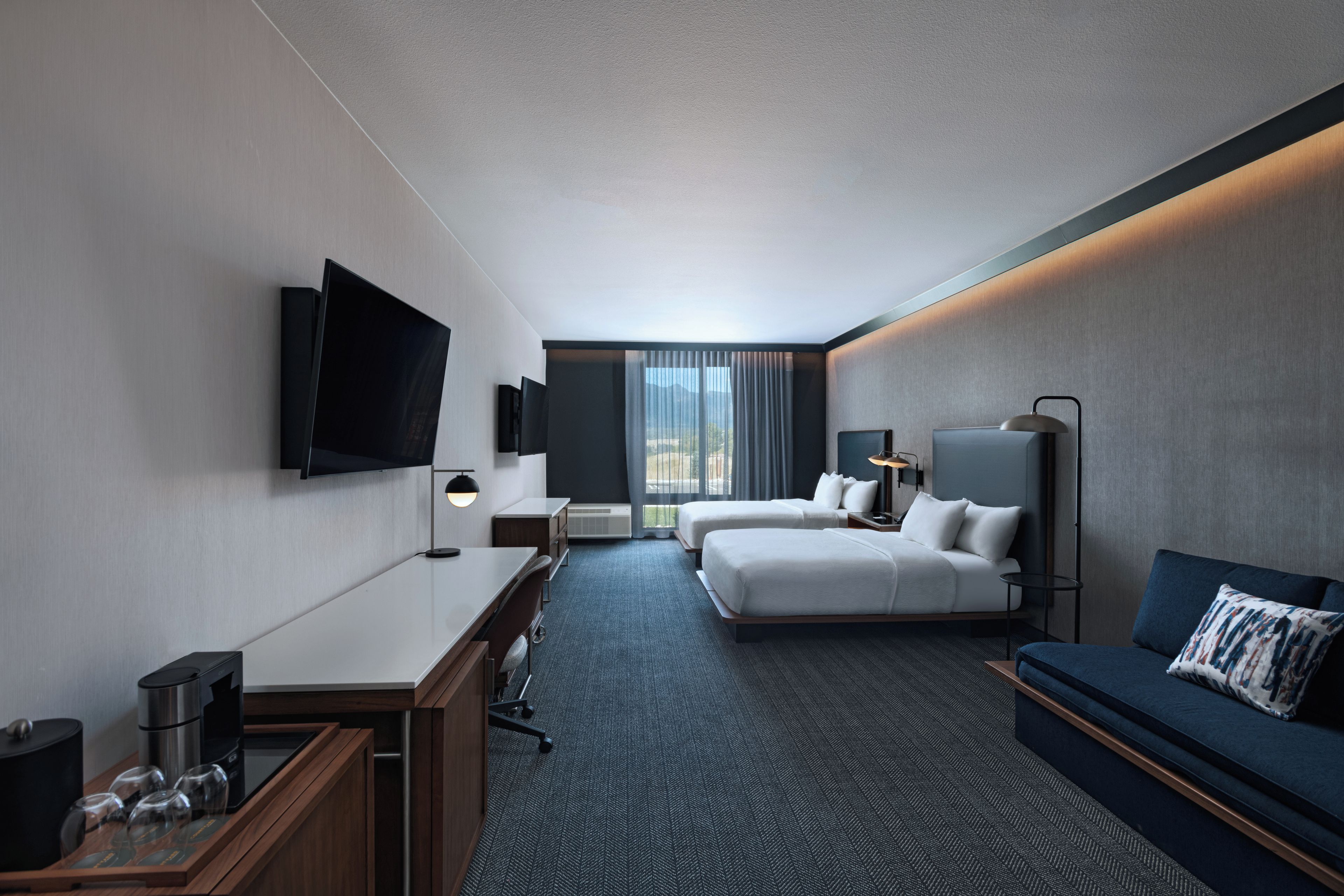 A hotel room with a bed, a desk, a TV, a sofa, and a window with curtains.