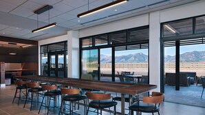 Zona de bar moderna con una larga barra de madera, varios taburetes y ventanas amplias con vistas a la montaña.