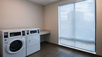 A laundry area with two front-loading washing machines, a small countertop, and a large window with a city view.