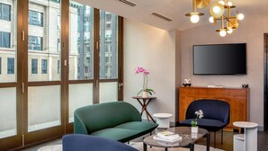 A modern living room with large windows, a flat-screen TV, and a green sofa. - Le Meridien New York, Fifth Avenue (New York)
