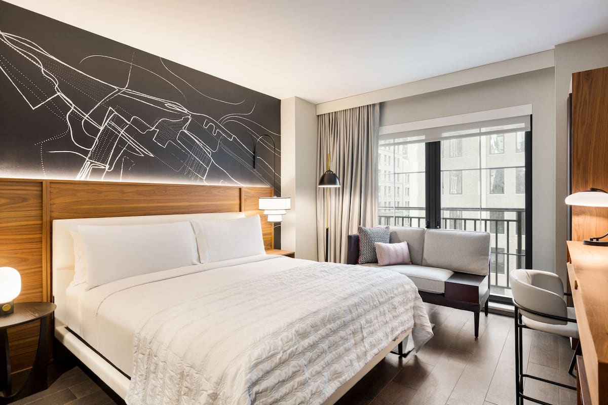 A modern hotel room with a large bed, a sofa, a desk, and a view of the city.