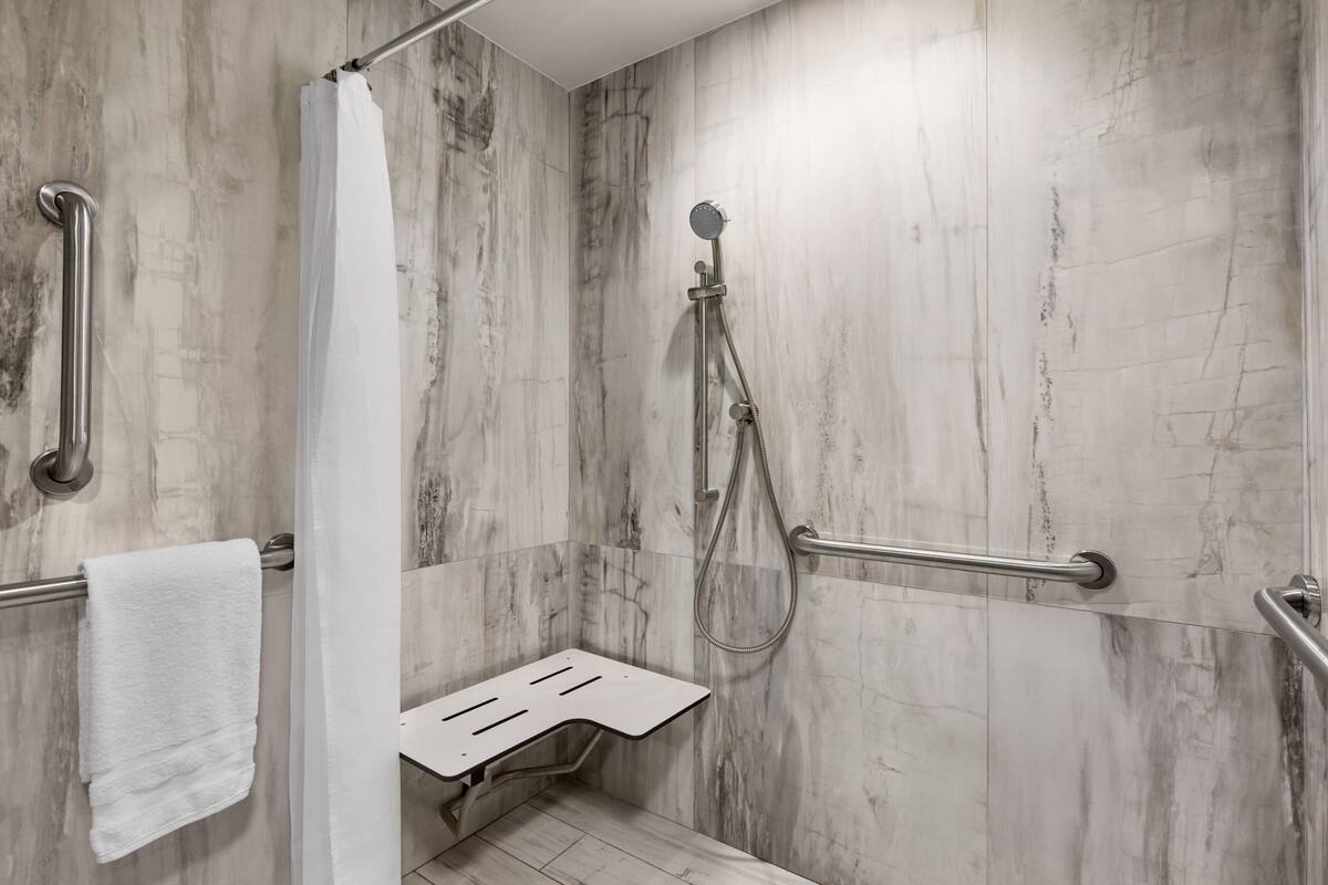 A modern bathroom with a shower, grab bars, and a white towel on a rack.