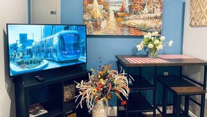 A living room with a TV displaying a cityscape, a painting of a landscape, and a table with a vase of flowers. - Luxe City Hall Suite by Rittenhouse Square (Philadelphia)