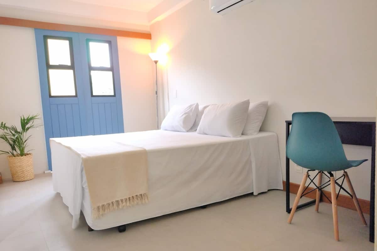 Un dormitorio con una cama, una silla, una planta en maceta y una puerta.