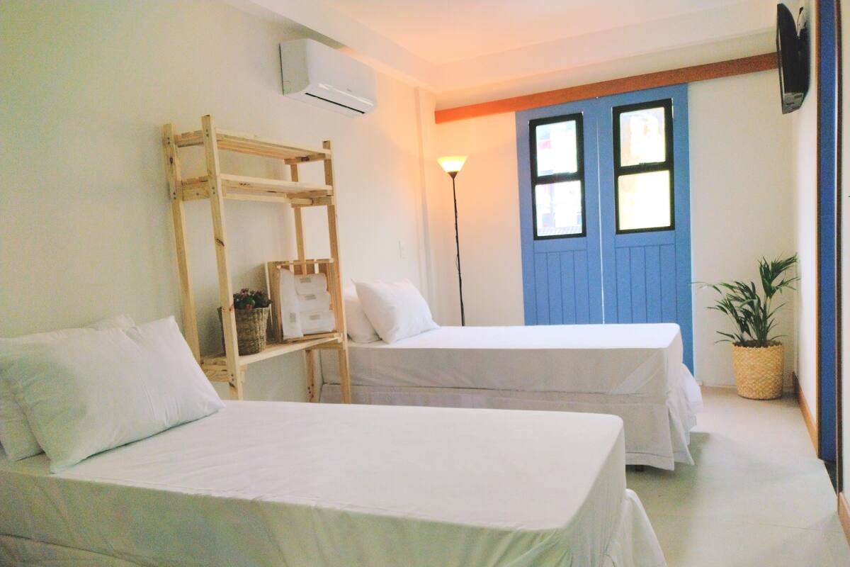 Una habitación con dos camas, una escalera de madera, una puerta azul y una lámpara de pie.