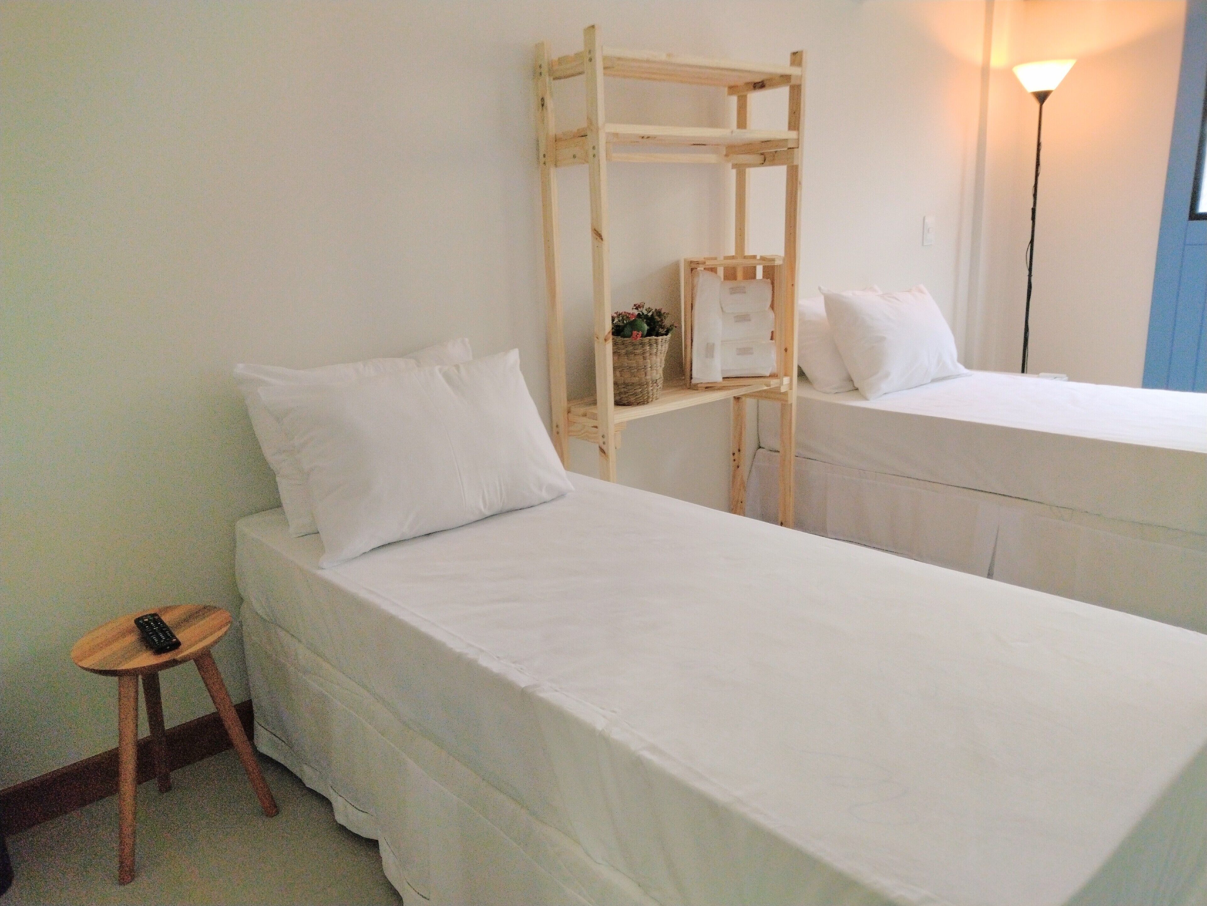 A simple room with two beds, a small wooden shelf with a basket, and a remote control on a stool.