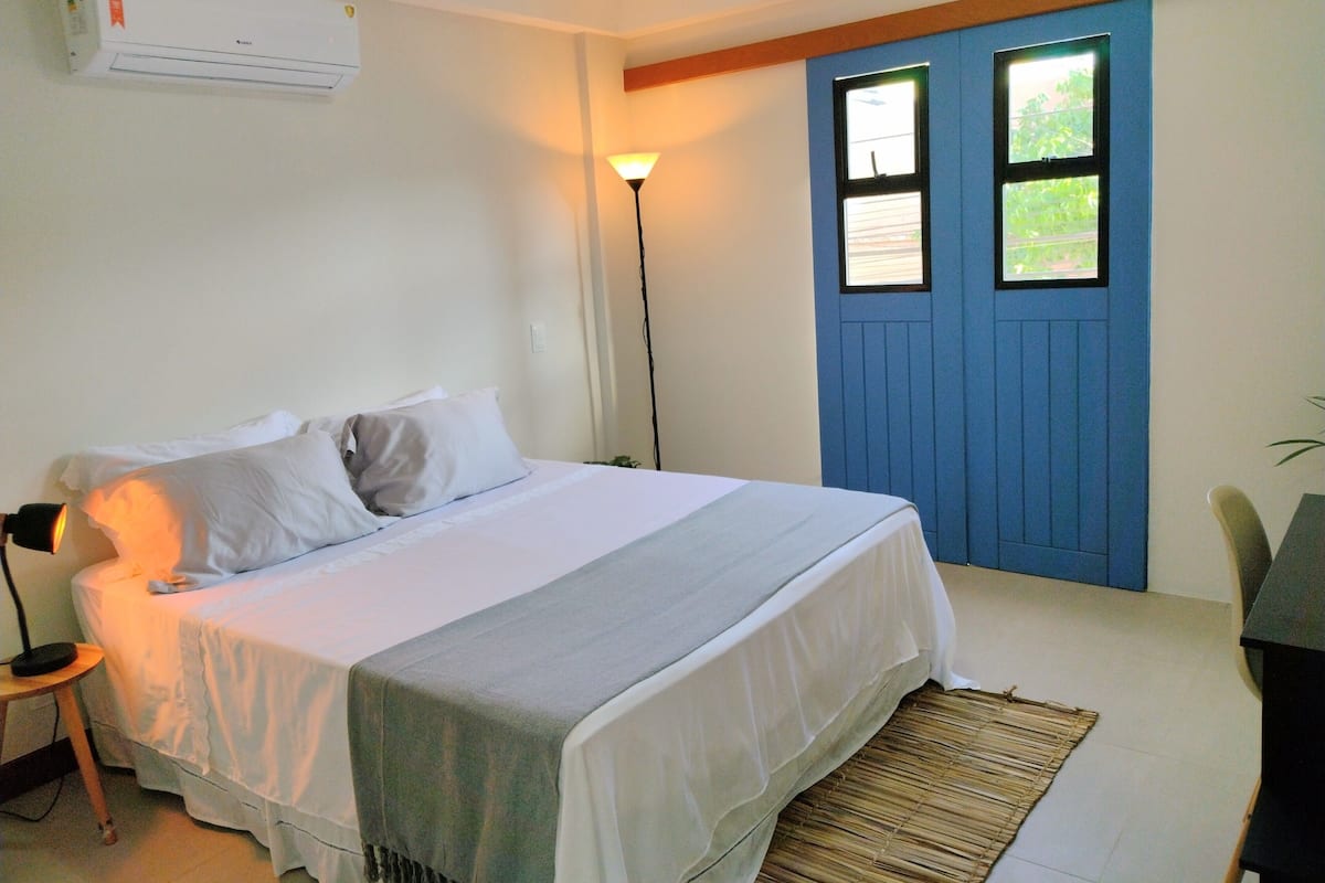 Un dormitorio con cama, lámpara de noche, aire acondicionado y una puerta azul.
