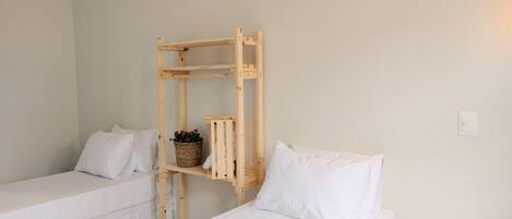 Quarto com duas camas individuais, uma estante de madeira com cesta e um ar condicionado branco na parede.