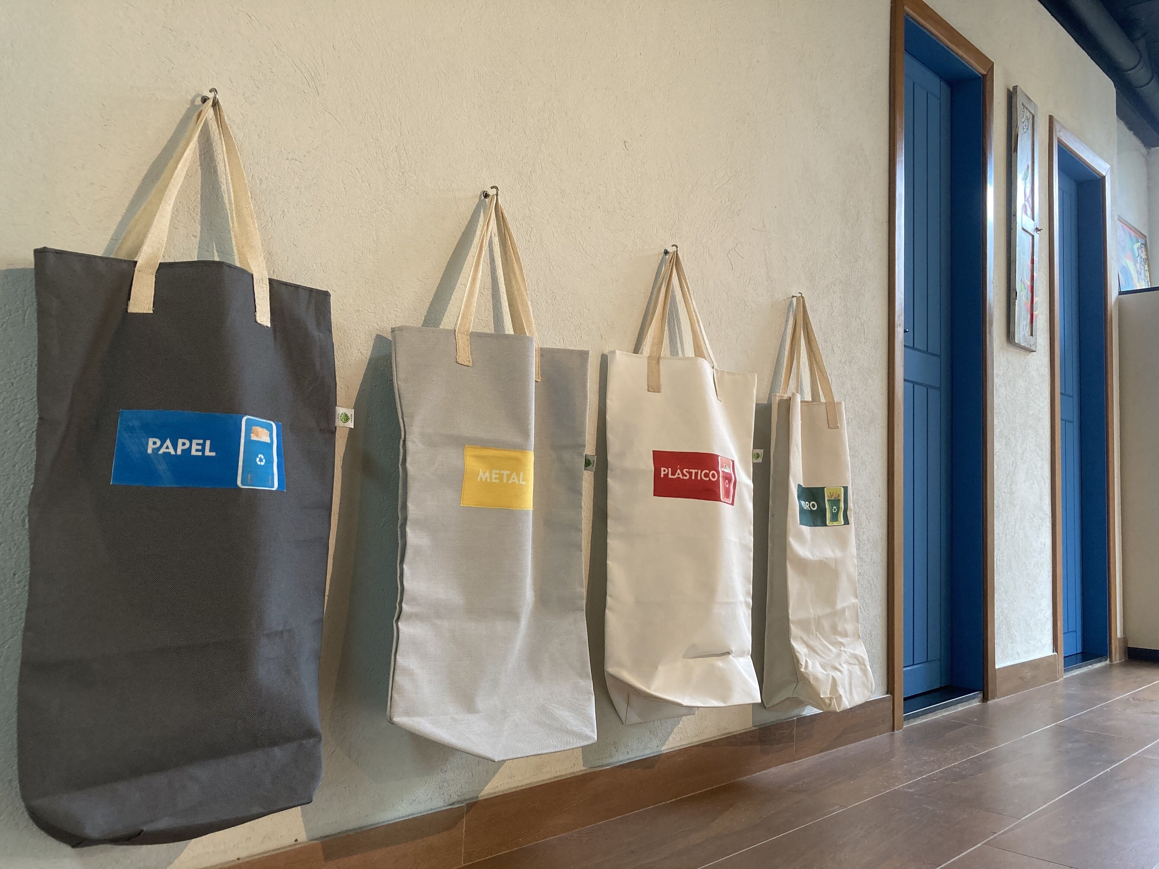 Four tote bags hanging on a wall, each with a different label.