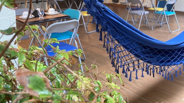 Una habitación con una hamaca azul, sillas azules y amarillas, una mesa de madera y una escalera al fondo.